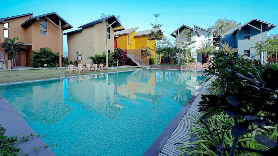 An image of a swimming pool surrounded by houses and trees - Pride Resort Ambaji